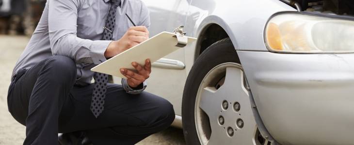 a man crouched down taking notes on a clipboard next to a car